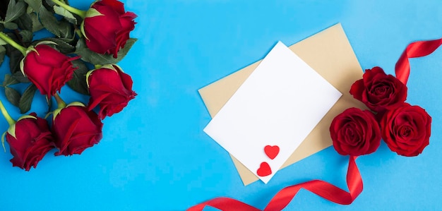 Holiday banner Top view of empty white paper for text red roses and hearts on the blue background Copy space