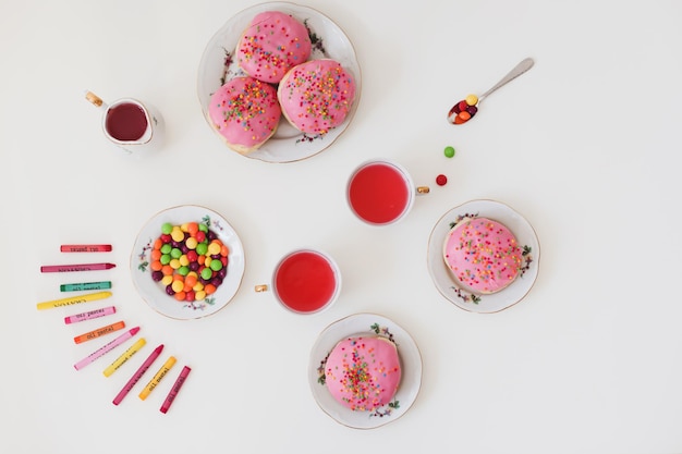 праздничная композиция для вечеринки по случаю дня рождения с разноцветными пончиками в розовой глазури на белом плоском виде сверху