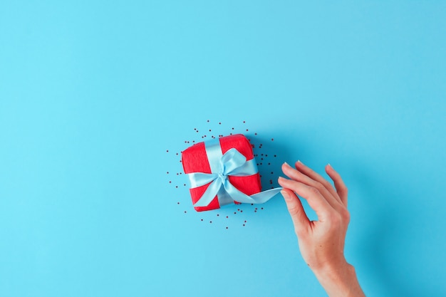 Holiday blue background with woman hand opening red gift