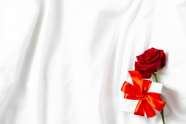 Holiday card top view red rose and box with gift on white bed Valentine background Happy Mothers day Happy womens day Happy birthday Good morning Marriage proposal