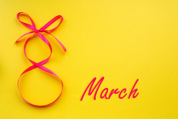 写真 黄色の背景に8の字の形をしたピンクのリボンが付いたホリデーカード、国際女性の日