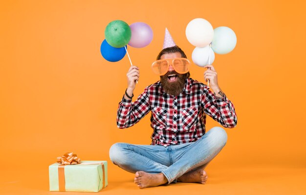 Holiday celebration bearded mature man celebrate birthday party cheerful man in bday hat hold holiday balloons gifts and presents concept have a happy holiday party time happy birthday to you