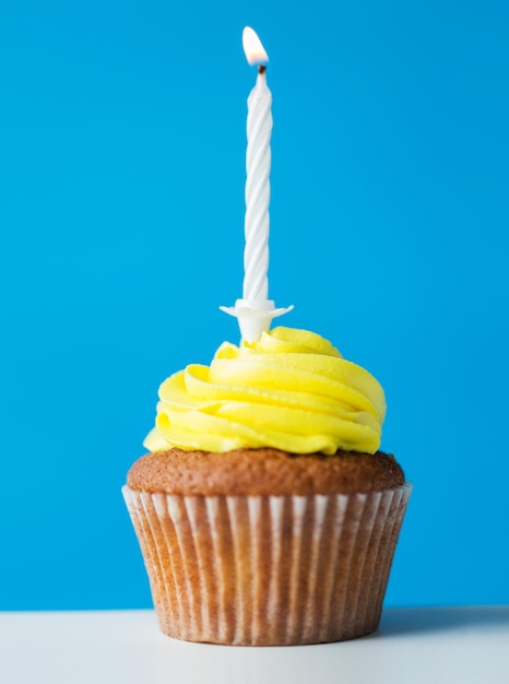 holiday, celebration, greeting and party concept - birthday cupcake with one burning candle over blue background