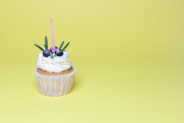 Holiday, celebration, greeting and party concept - birthday cupcake with one burning candles over yellow background