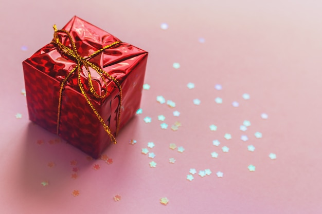 Holiday christmas birthday greeting card. Present red gift box with golden bow ribbon on pink background. Bright shining glitter bokeh background. Copyspace for text