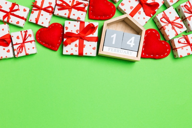 Holiday composition of gift boxes, wooden calendar and red textile hearts on colorful background with empty space for your design. The fourteenth of February. Top view of Valentine's Day concept