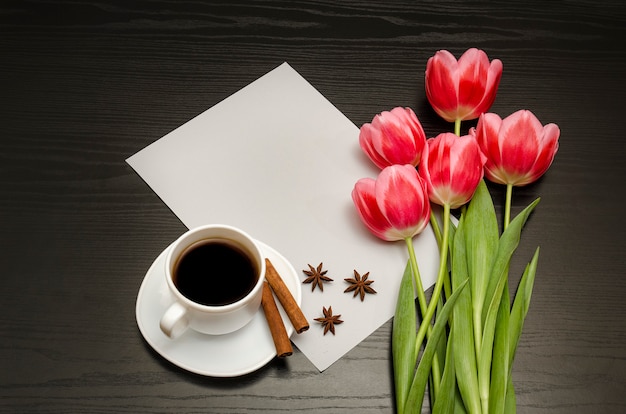 Concetto di vacanza. mazzo di tulipani rosa, una tazza di caffè, cannella, anice stellato e foglio di carta su legno nero