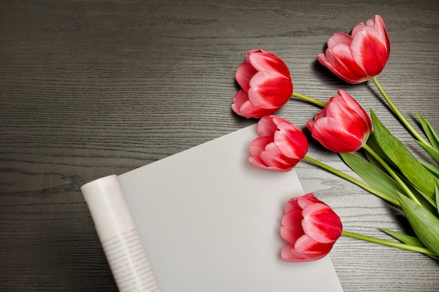 Holiday concept. Bouquet of pink tulips and piece of paper on black wood