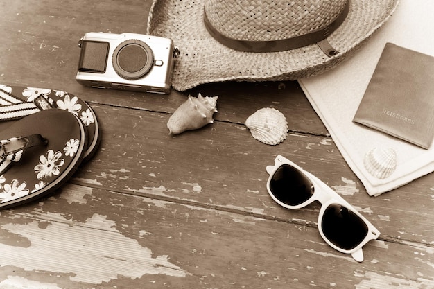 Concetto di vacanza tavolo in legno vintage con accessori per le vacanze occhiali da sole con cappello di paglia infradito conchiglie asciugamano e passaporto per fotocamera vintage