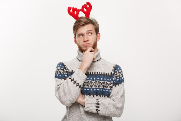 Holiday concept young beard man in sweater with thoughtful gesture on white background