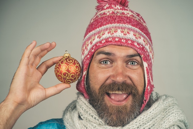 Holiday decorations and ornaments bearded hipster in winter hat and scarf holds decoration new years