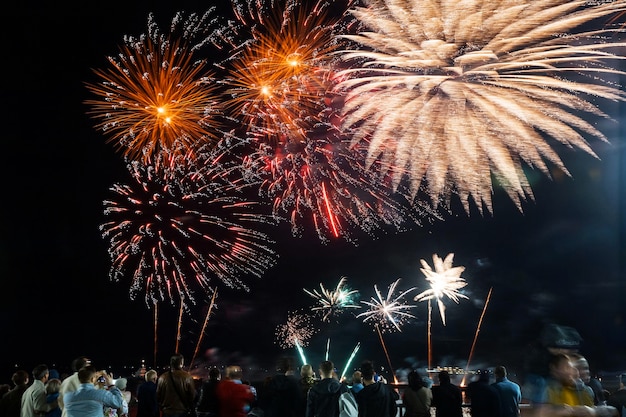 Holiday fireworks on the black sky background above silhouettes of people