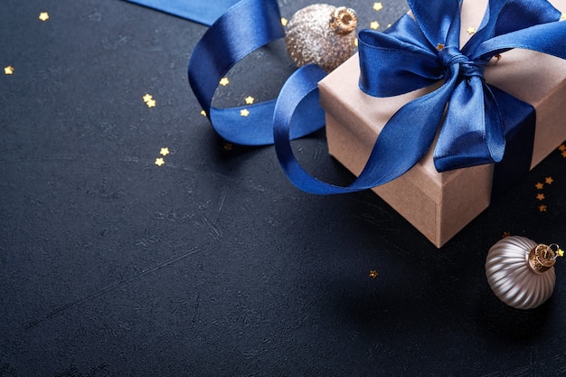 Holiday gift box or present with blue ribbon, golden confetti and gold baubles on black background. Magic christmas greeting card. Christmas Decoration. Border design. Mock up. Top view.