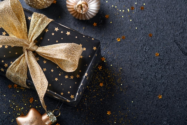 Праздничная подарочная коробка или подарок с лентой, золотым конфетти и золотыми шарами на черном фоне. Волшебная рождественская открытка. Рождественские украшения. Бордюрный дизайн. Макет. Вид сверху.