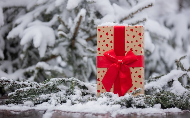 Holiday gift box with heart shapes on wooden table in snow