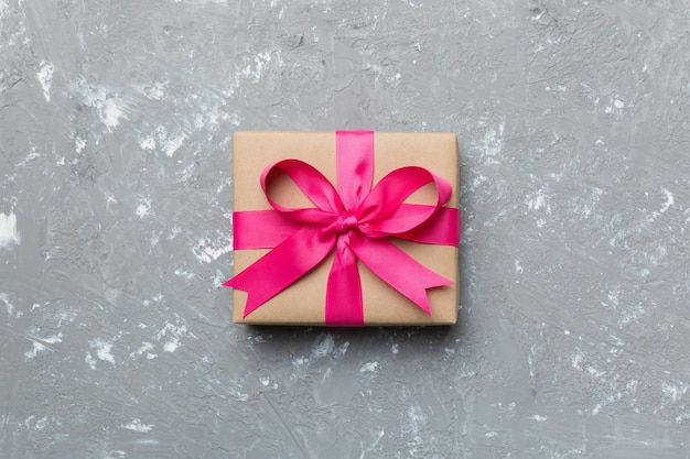 Holiday gift box wrapped in craft paper with colored bow on table background Top view flat lay copy space