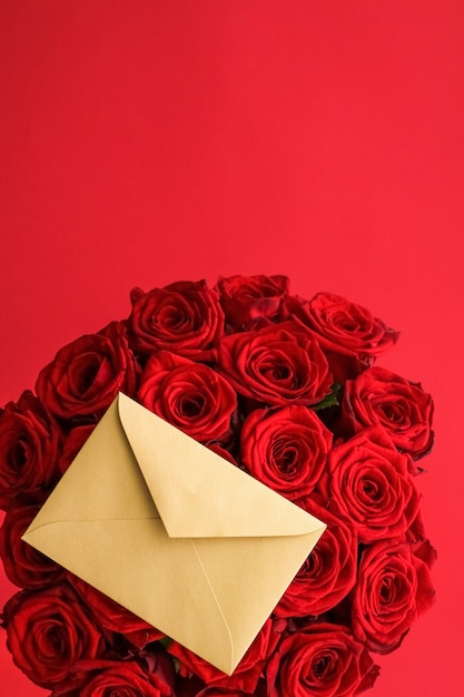 Holiday gift flowers flatlay and happy relationship concept  love letter and flower delivery service on valentines day luxury bouquet of red roses and card envelopes on red background