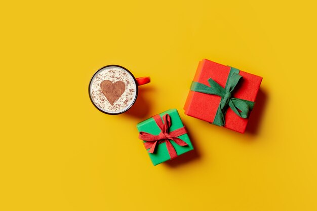 Holiday gifts and cup of coffee with heart shape on yellow background. Top view