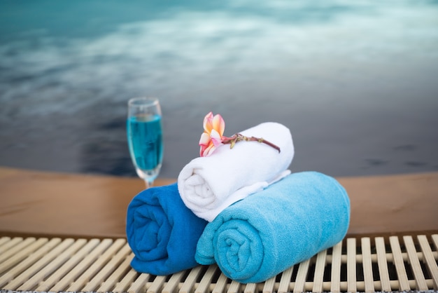 Photo holiday glass of white wine and towel by swimming pool.