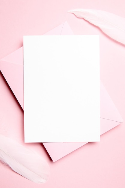 Photo holiday greeting card mockup with pink envelope and white feather on light pink background top view flat lay blank wedding invitation or valentine day letter empty card