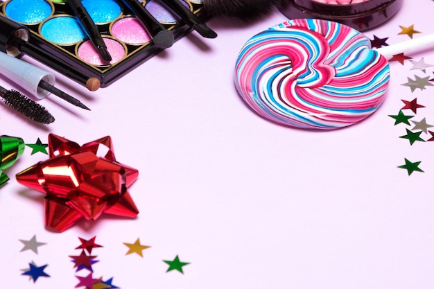 Holiday party makeup products with lollipop confetti and gift wrap bows Copy space