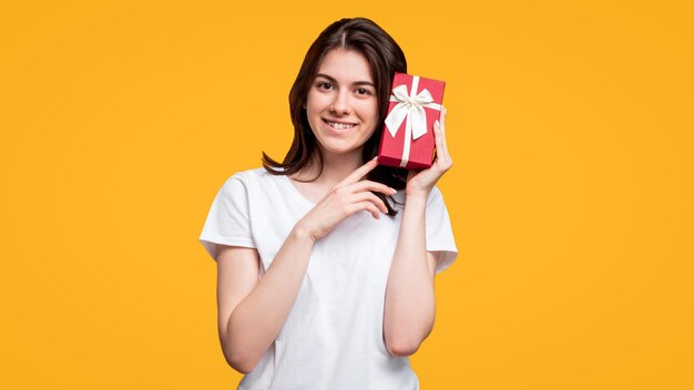 Holiday present Birthday surprise Happy cheerful woman in white tshirt holding red gift box isolated on orange copy space Festive occasion