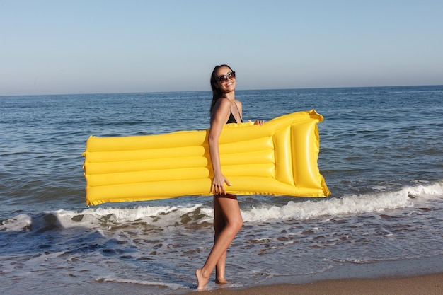 ホリデーリゾート観光コンセプト夏の晴れた日にビーチで膨脹可能なドーナツと一緒に泳ぐ女性