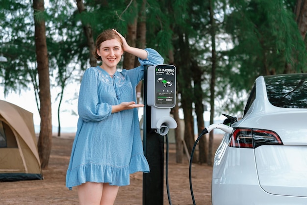 電気自動車でビーチキャンプ旅行の休暇 若い女性がグリーンでクリーンなエネルギーでEV車を充電 エコフレンドリーなEV車でビーチキャンプ旅行 永久