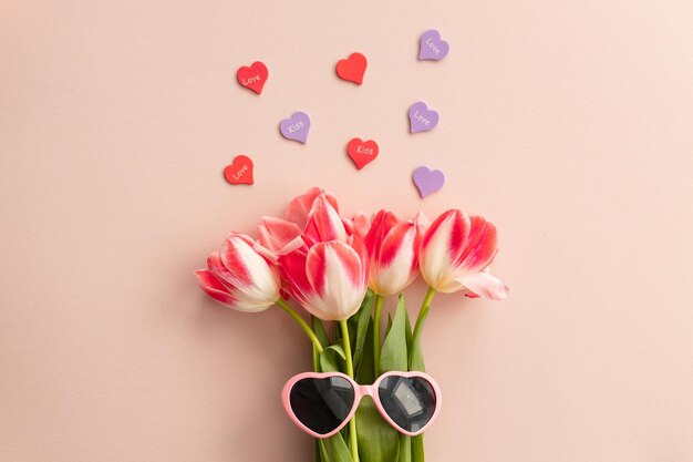 Photo holiday and spring concept top view photo of bouquet of pink tulips and pink sunglasses