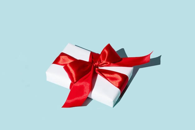 Holiday surprise. Women day. Long-distance gift. Care package. Present wrapped in white box with red ribbon bow isolated on blue copy space background.