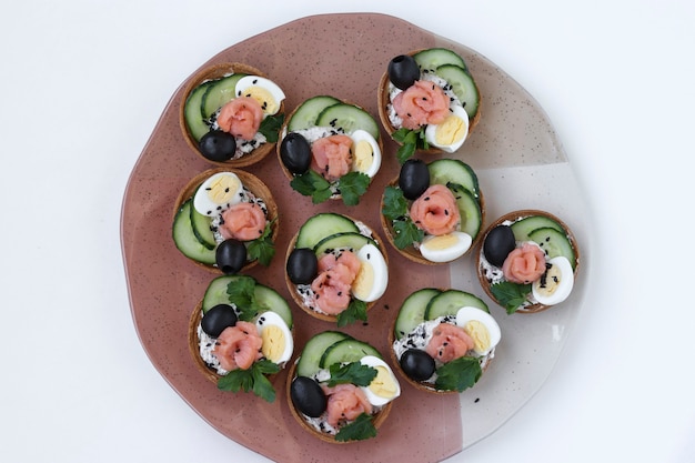 Holiday tartlets with cheese, salmon, black olives, quail eggs and cucumbers on a plate on white background, Top view, Closeup