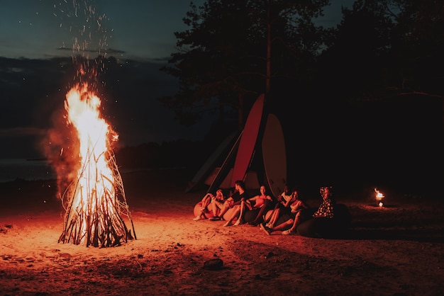 Holiday Time Company Sit In Front Of Bonfire On Beach.