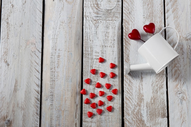 Holidays background : on white background white watering can and red hearts . 