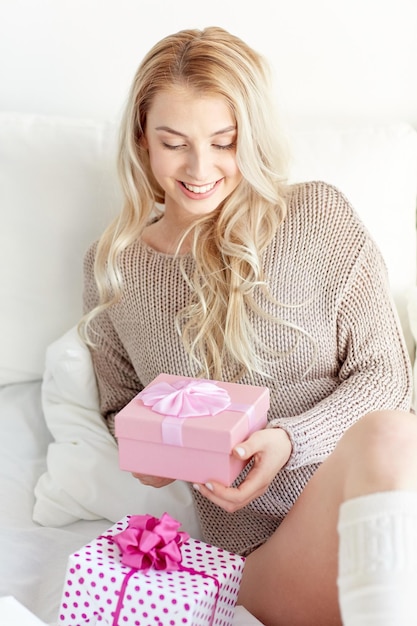 holidays, birthday, morning and people concept - happy young woman gift boxes or presents in bed at home bedroom