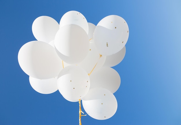 Holidays, birthday, party and decoration concept - close up of inflated white helium balloons in blue sky