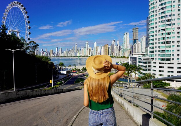 Holidays in brazil rear view of young woman with hat enjoying balneario camboriu city skyline santa catarina brazil