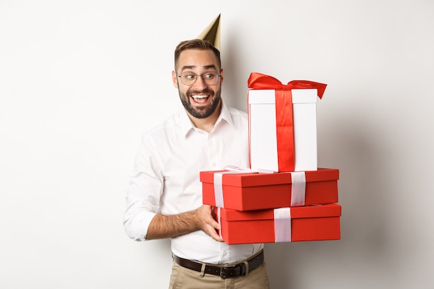 Feste e celebrazioni. uomo eccitato che ha festa di compleanno e riceve regali, guardando felice, in piedi su sfondo bianco.