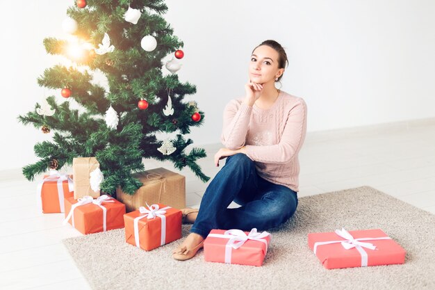 休日、お祝い、お祭りのコンセプト-クリスマスツリーの下に座っている美しい若い女性