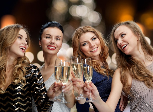 holidays, celebration and people concept - happy women clinking non alcoholic champagne glasses at new year party over christmas tree lights background