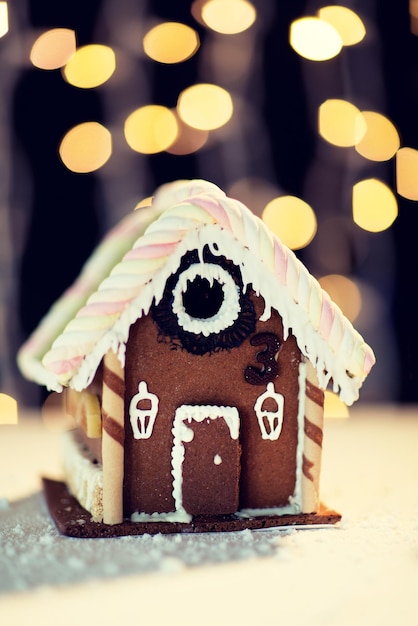 концепция праздников, рождества, выпечки и сладостей - крупный план красивого пряничного домика на столе над черными гирляндами