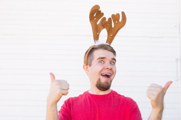 Holidays and christmas concept - Young man in deer's horns with thumb up gesture on white background.