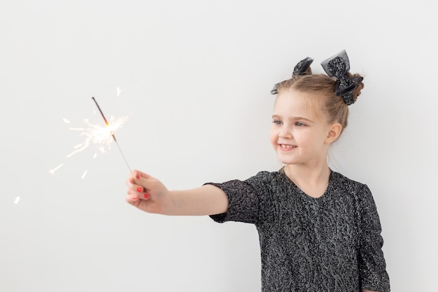 Holidays, christmas and new year concept - Happy child holds burning sparkler in her hand over white background with copy space.