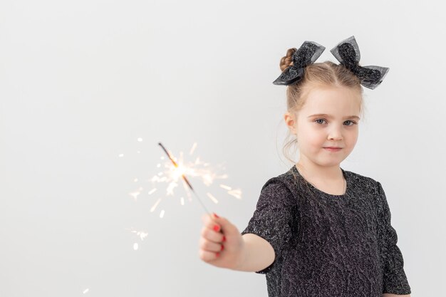 Holidays, christmas and new year concept - Happy child holds burning sparkler in her hand over white background with copy space.