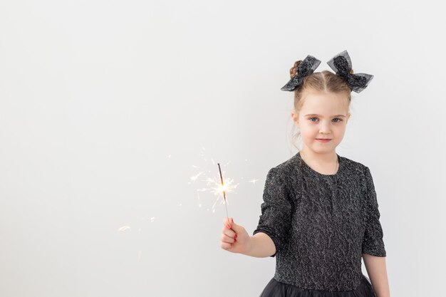 Holidays, christmas and new year concept - Happy child holds burning sparkler in her hand over white background with copy space.