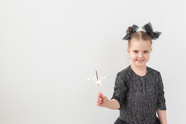 Holidays, christmas and new year concept - Happy child holds burning sparkler in her hand over white background with copy space.