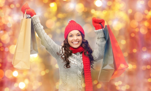 Фото Праздники, рождество, распродажа и концепция людей - счастливая улыбающаяся молодая азиатка в зимней одежде с сумками для покупок на фоне огней