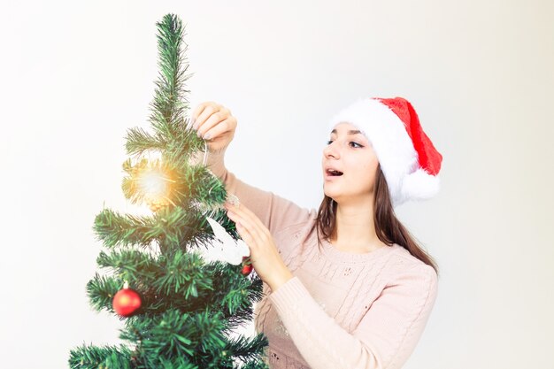 休日のコンセプト-サンタの帽子をかぶった女の子がクリスマスツリーを飾りました。クリスマスを待っています。