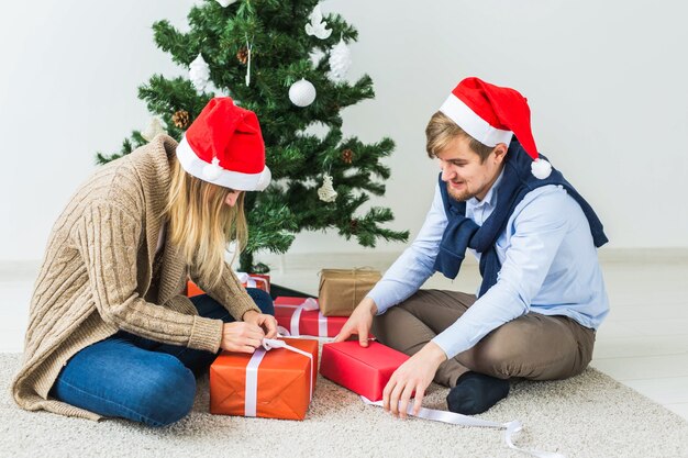 Holidays concept - Sweet couple opening Christmas gifts, sitting in the living room.