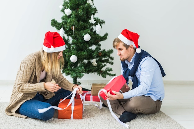 휴일 개념 - 크리스마스 선물을 여는 달콤한 커플은 거실에 앉아 있습니다.