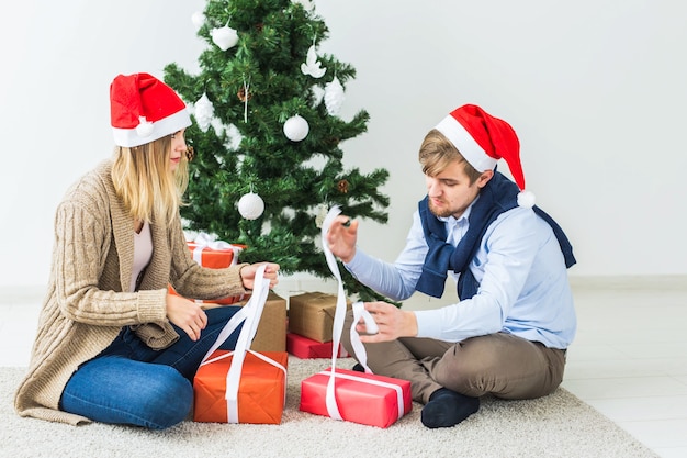 Holidays concept - Sweet couple opening Christmas gifts, sitting in the living room